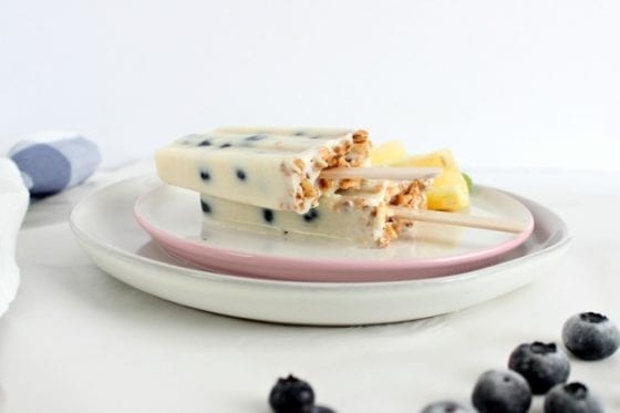 easy blueberry yogurt popsicles with granola on two plates with blueberries and lemos