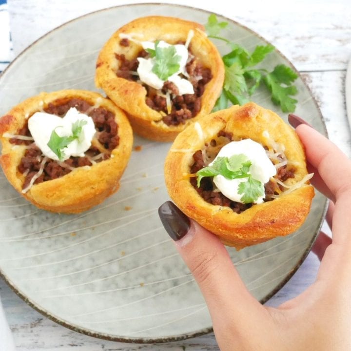 BBQ-Beef-Croissant-Cups in a plate with cilatro, a dollop of sour cream, and melted cheese grabbed by hand