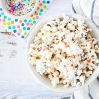 white chocolate popcorn with rainbow colors sprinkles, colorful polka-dots napking and white and blue stripes kitchen towel