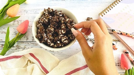 chocolate popcorn, hand picking popcorn from a white bowl, tulip flowers on the side, kitchen towel, pen, calendar on another side