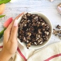 chocolate popcorn in a white bowl, hand holding the glass bowl, tulip flowers, kitchen towel, planner and pen over a wood counter