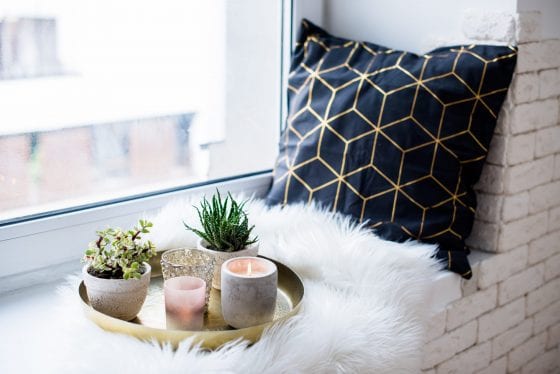 decor tray filled with candles, cactus plants and a glass drink, with a black pillow on the side over a fur blanket