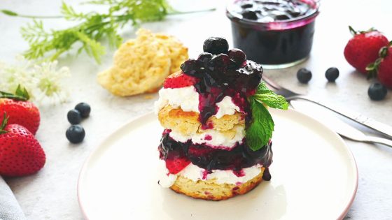 strawberry shortcake with lemon biscuits, blueberry lemon sauce, fresh strawberries in a white and pink plate, fresh blueberries and a kitchen napkin