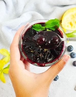 blueberry lemon sauce in a glass jar with mint leaf, lemons, yellow flowers, fresh blueberries, kitchen towel