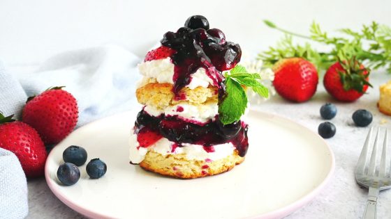 strawberry shortcake with lemon biscuits, blueberry lemon sauce, fresh strawberries in a white and pink plate, fresh blueberries, utensils, and a kitchen napkin
