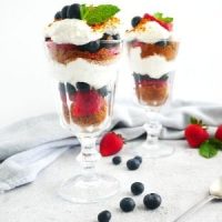 easy no-bake cheesecake, berries and biscoff crust parfaits served on tall glasses with long dessert spoon and kitchen napkin on the side