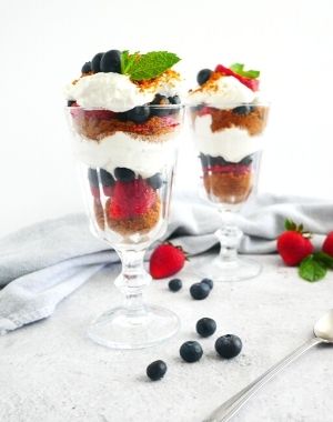 easy no-bake cheesecake, berries and biscoff crust parfaits served on tall glasses with long dessert spoon and kitchen napkin on the side